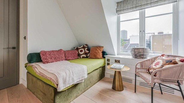 Een slaapkamer met een bed, een stoel, een raam en uitzicht op gebouwen.