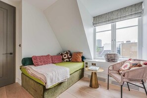 Une chambre à coucher avec un lit, une chaise, une fenêtre et une vue sur des immeubles.