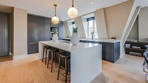 Een moderne keuken met een centraal eiland, barkrukken, hanglampen en uitzicht op de stad.