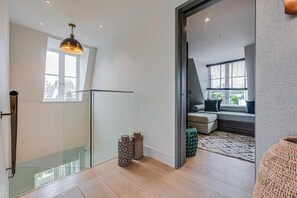 A modern interior with a glass door leading to a living area, a hanging light fixture, and patterned stools. - Four Bedroom Duplex Penthouse (London)