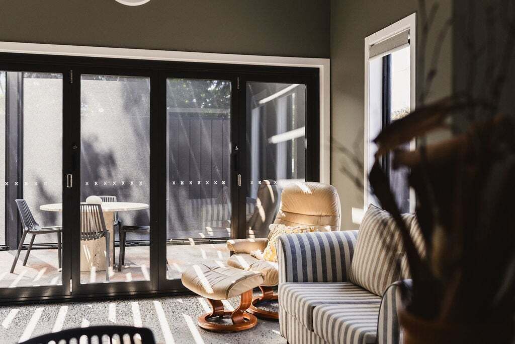 A modern living room with a large sliding glass door leading to an outdoor area, featuring a sofa, armchair, and a small table.
