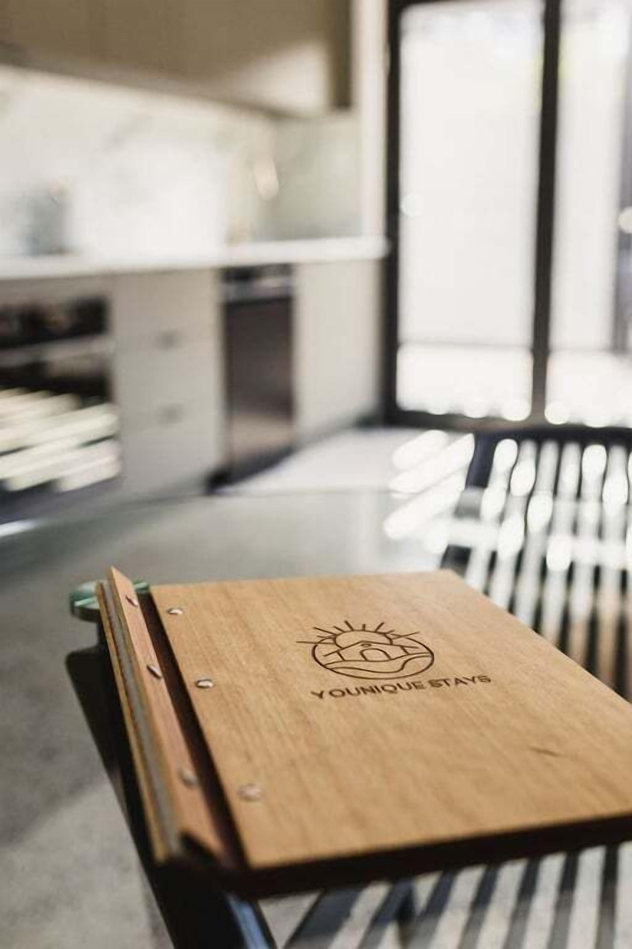 A wooden table with a logo and text, set in a modern kitchen with striped chairs and a large window.