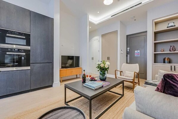 A modern kitchen with built-in appliances, a dining area with a coffee table, and a seating area with a sofa and armchairs. - Two-Bedroom Superior Apartment (London)