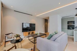 Un salon moderne avec un téléviseur à écran plat, un canapé, une table basse et une petite table d’appoint agrémentée d’une plante.