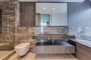 Een moderne badkamer met een marmeren wand, een inbouw wastafel, een toilet en een grote spiegel.