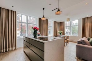 A modern kitchen with a central island, large windows, and a dining area with a sofa. - Two-Bedroom Superior Apartment (London)