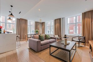 A modern living room with a sofa, coffee table, and dining area. - Two-Bedroom Superior Apartment (London)