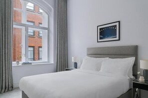 Hotelkamer met een groot bed, nachtkastje met lamp, een lijst aan de muur en een raam met gordijnen.