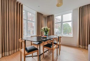 A dining area with a table and chairs, large windows, and curtains. - Two-Bedroom Superior Apartment (London)