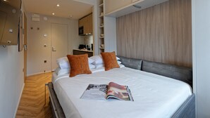 Ein modernes Hotelzimmer mit einem großen Bett, einer Zeitschrift auf dem Bett und einer Küchenzeile im Hintergrund.