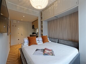 A modern hotel room with a large bed, a magazine on the bed, and a kitchenette in the background. - Standard Studios in South Kensington (London)