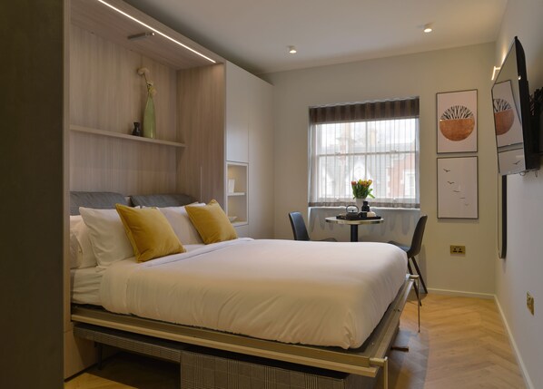 Une chambre à coucher moderne, avec un lit, des tables de chevet, une petite table ronde avec des chaises et des œuvres d’art accrochées aux murs.