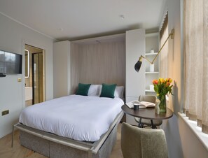 A modern hotel room with a bed, bedside table, and a TV mounted on the wall. - Standard Studios in South Kensington (London)