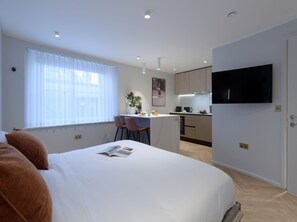 A modern hotel room with a large bed, a small desk, and a kitchen area. - Standard Studios in South Kensington (London)