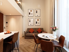 A modern living room with a sofa, two orange cushions, a round coffee table, and a vase with flowers. - Duplex One Bedroom Apartment (London)
