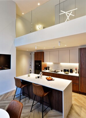 A modern kitchen with a central island, bar stools, and a built-in oven. - Duplex One Bedroom Apartment (London)