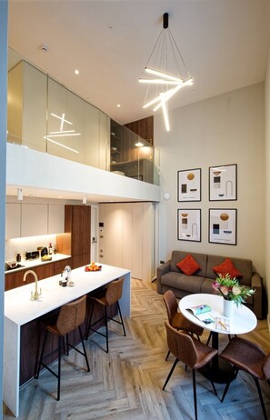 A modern kitchen with a central island, a dining area with chairs, and a living space with a sofa and cushions. - Duplex One Bedroom Apartment (London)