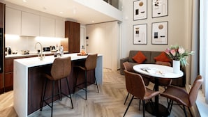 Una cocina moderna con una isla central, taburetes de bar y una mesa de comedor con sillas. Hay obras de arte enmarcadas en la pared y un jarrón con flores sobre la mesa del comedor.