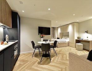 Una habitación de hotel moderna con kitchenette, comedor, cama y escritorio con lámpara.