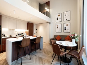 Una cocina moderna con una isla central, taburetes de bar y una mesa de comedor con sillas. Hay obras de arte enmarcadas en la pared y un jarrón con flores sobre la mesa del comedor.