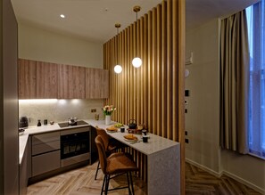 Una cocina moderna con armarios de madera, encimera de mármol, horno empotrado y comedor con dos sillas.