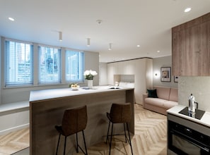 A modern kitchen with a central island, bar stools, and a built-in oven. - Superior Studio in Notting Hill (London)