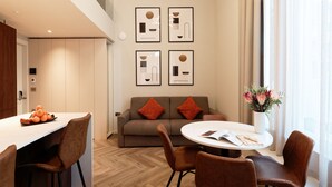 Een moderne woonkamer met een bank, twee oranje kussens, een ronde salontafel en een vaas met bloemen.