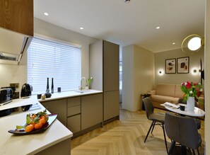 A modern kitchen with a sink, countertop, and a dining area with a table and chairs. - Superior Studio in Notting Hill (London)
