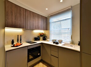 A modern kitchen with wooden cabinets, a built-in oven, a sink, and a window with blinds. - Superior Studio in Notting Hill (London)