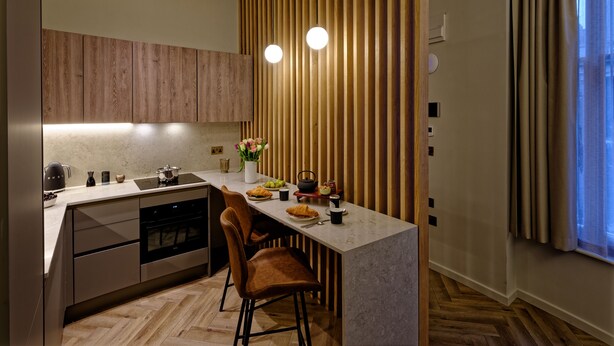 Een moderne keuken met houten kastjes, een marmeren aanrecht, een inbouwoven en een eethoek met twee stoelen.