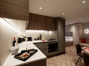 A modern kitchen with a built-in oven, a coffee machine, and a dining area with a chair and table. - Superior Studio in Notting Hill (London)