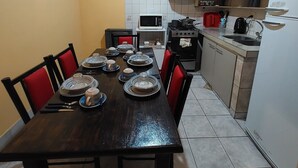 A dining area with a wooden table set for four, red chairs, a kitchen with a stove, microwave, and cabinets. - Aparment Camila 2 (El Calafate)