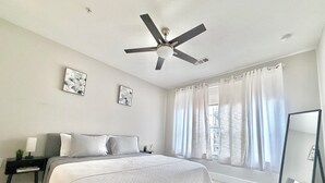 A bedroom with a bed, a ceiling fan, a window with curtains, and a mirror. - Luxury buckhead apartment (Atlanta)