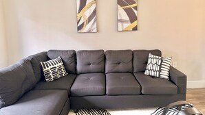Ein modernes Wohnzimmer mit Ecksofa, zwei abstrakten Gemälden und dekorativen Kissen mit Muster.
