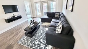 Ein modernes Wohnzimmer mit einem schwarzen Ecksofa, einem flachbildfernseher an der Wand und einem Deckenventilator.