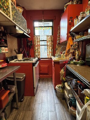 Cocina compacta con armarios rojos, una ventana con cortinas estampadas y diversos electrodomésticos.