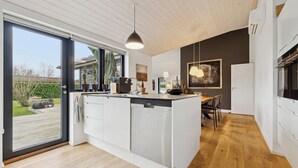 Una cucina moderna con un'isola grande, un'area pranzo con sedie e una vista attraverso una porta scorrevole in vetro.