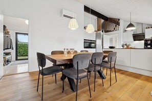 A modern kitchen with a wooden dining table, grey chairs, pendant lights, and a large island with a microwave. - New holiday home close to the beach (Middelfart)