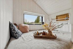 A cozy attic room with a window, a wooden shelf, a fluffy pillow, a tray with decorative items, and a vase with dried flowers. - New holiday home close to the beach (Middelfart)