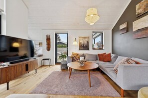 Een moderne woonkamer met een flatscreen televisie, een houten kast, een grijze bank en een ronde salontafel.