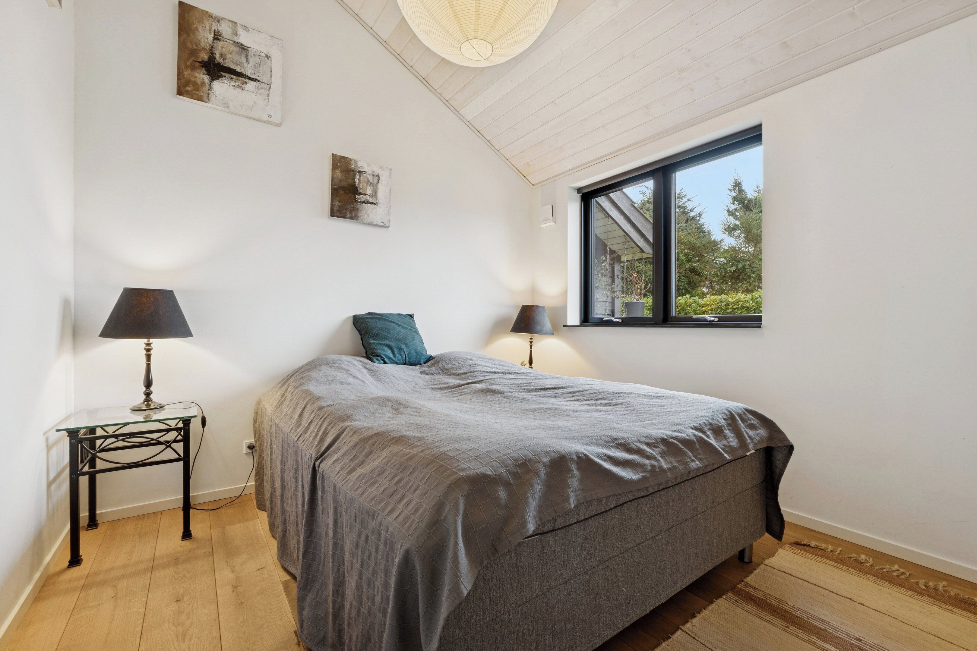 Une chambre à coucher avec un lit, deux lampes de chevet, une fenêtre et un luminaire au plafond.