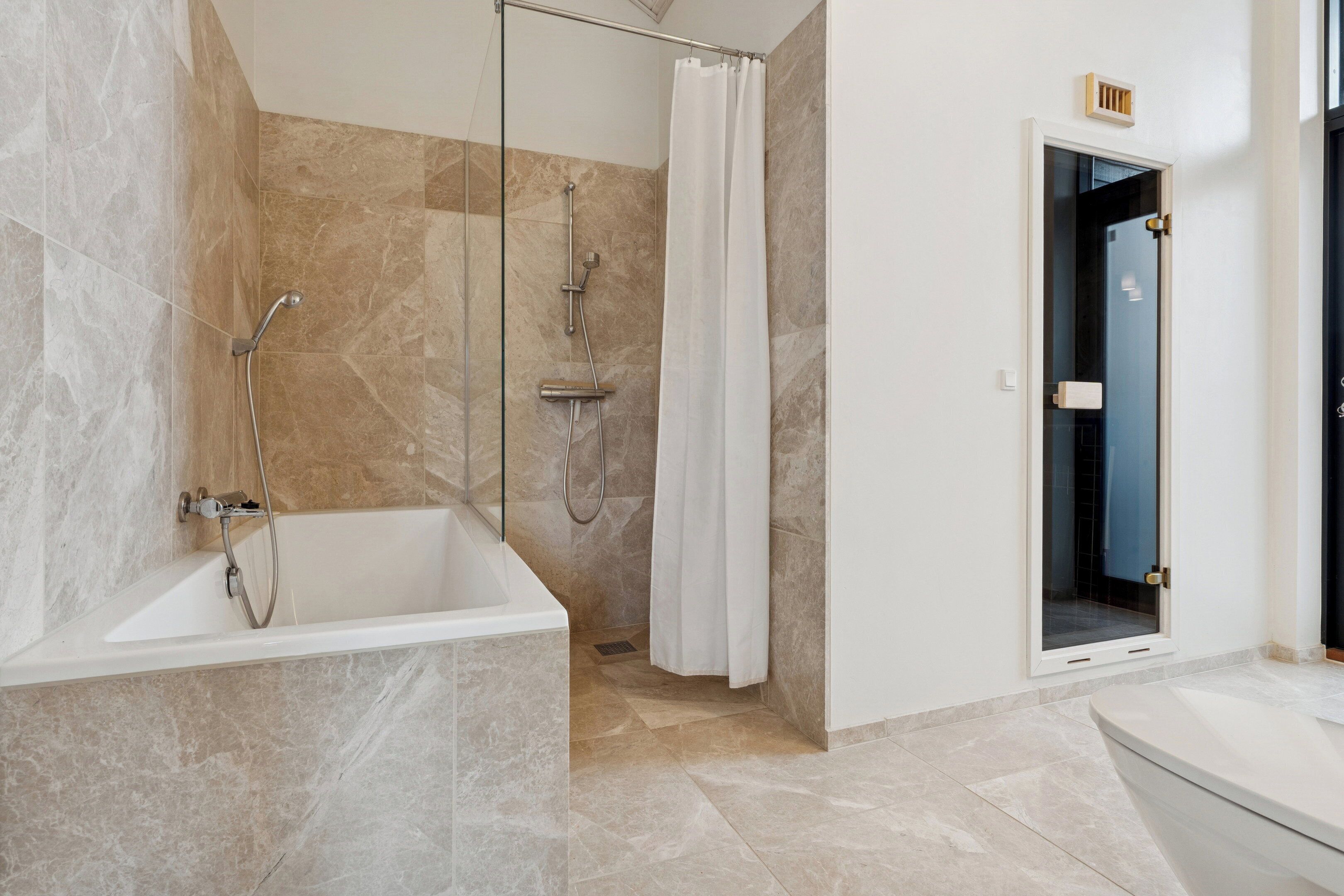 Une salle de bain moderne dotée d’une douche à parois de verre, d’une baignoire sur pieds et d’un espace toilettes séparé.