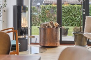 Een moderne woonkamer met een glazen haard, een gezellige zithoek en uitzicht op een tuin door grote ramen.