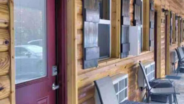 Fachada de madera con puerta roja, ventanas y asientos al aire libre.