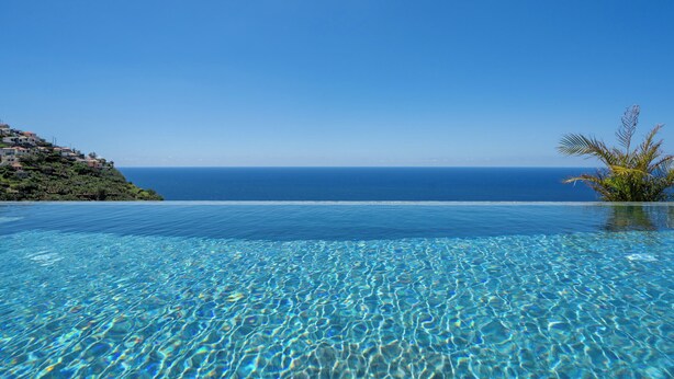 An infinity pool with clear blue water and a view of the ocean. - Calheta Hills IV – Apartment with Sea View (Calheta)