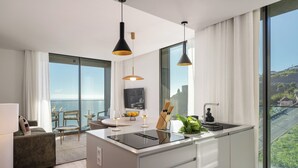 A modern kitchen with a central island, large windows, and a dining area with a view. - Calheta Hills IV – Apartment with Sea View (Calheta)
