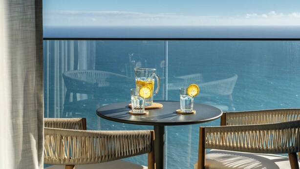 A table with drinks and chairs by a large window overlooking the ocean. - Calheta Hills IV – Apartment with Sea View (Calheta)
