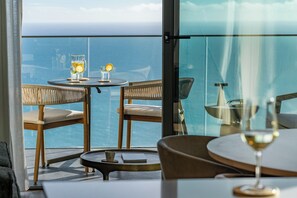 A balcony with wicker chairs, a round table, and a glass of wine. - Calheta Hills IV – Apartment with Sea View (Calheta)