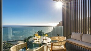 A balcony with a glass table, wicker chairs, and a sofa overlooking a coastal view. - Calheta Hills IV – Apartment with Sea View (Calheta)