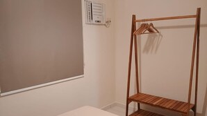 Ein schlichter Raum mit einer Holzhängeregalkombination, einem weißen Bett und einer Wandklimaanlage.